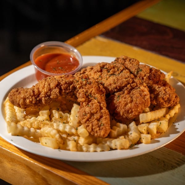 Crispy fried chicken tenders and crinkle-cut fries with a side of red dipping sauce.