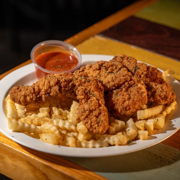 Crispy fried chicken tenders and waffle fries with a side of red dipping sauce.