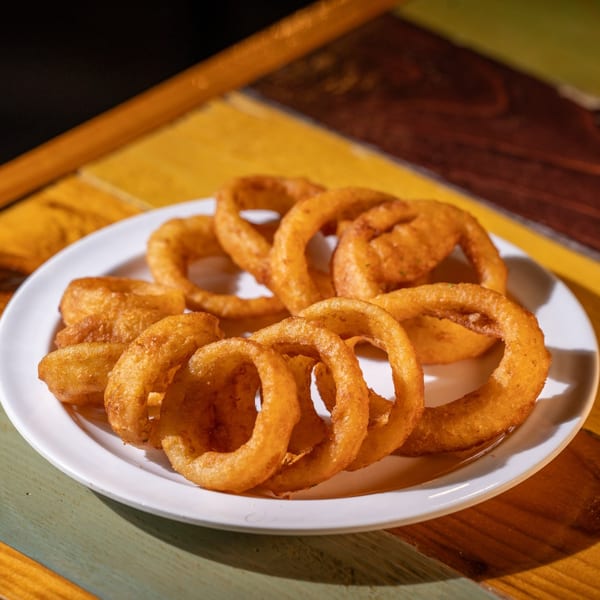 A white plate filled with golden-brown, crispy onion rings on a colorful wooden table.