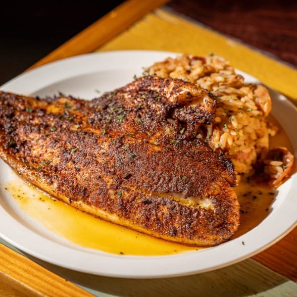 Blackened fish fillet with a side of jambalaya on a white plate at Nola Voodoo Tavern.