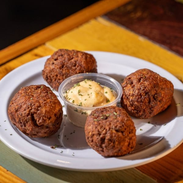 Four dark brown hushpuppies with a side of creamy dipping sauce on a white plate.