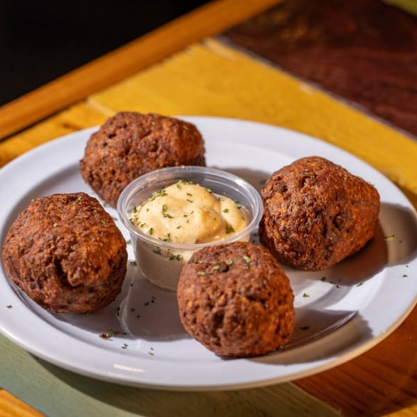 Four deep-fried boudin balls with a side of creamy dipping sauce on a white plate.