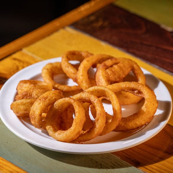 A white plate piled high with golden-brown, crispy onion rings on a colorful wooden table.